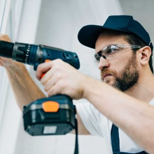 adult-repairman-in-goggles-fixing-window-handle-by-electric-drill-e1663969255653
